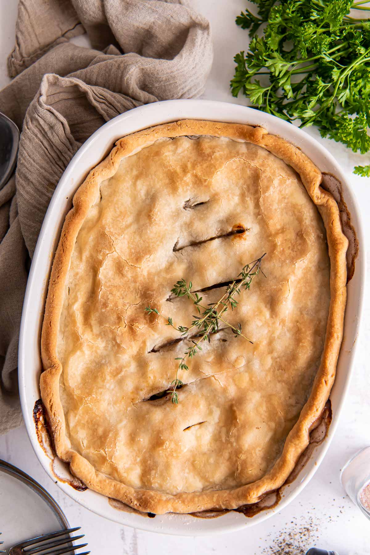 Ground Befef Pot Pie in an oval casserole dish with parsley and a taupe napkin on the side.