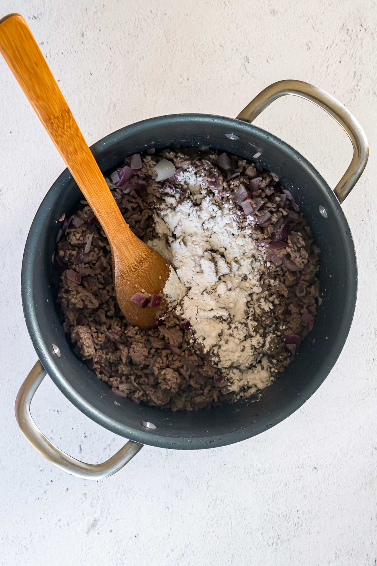 Flour sprinkled over cooked ground beef in a pot.