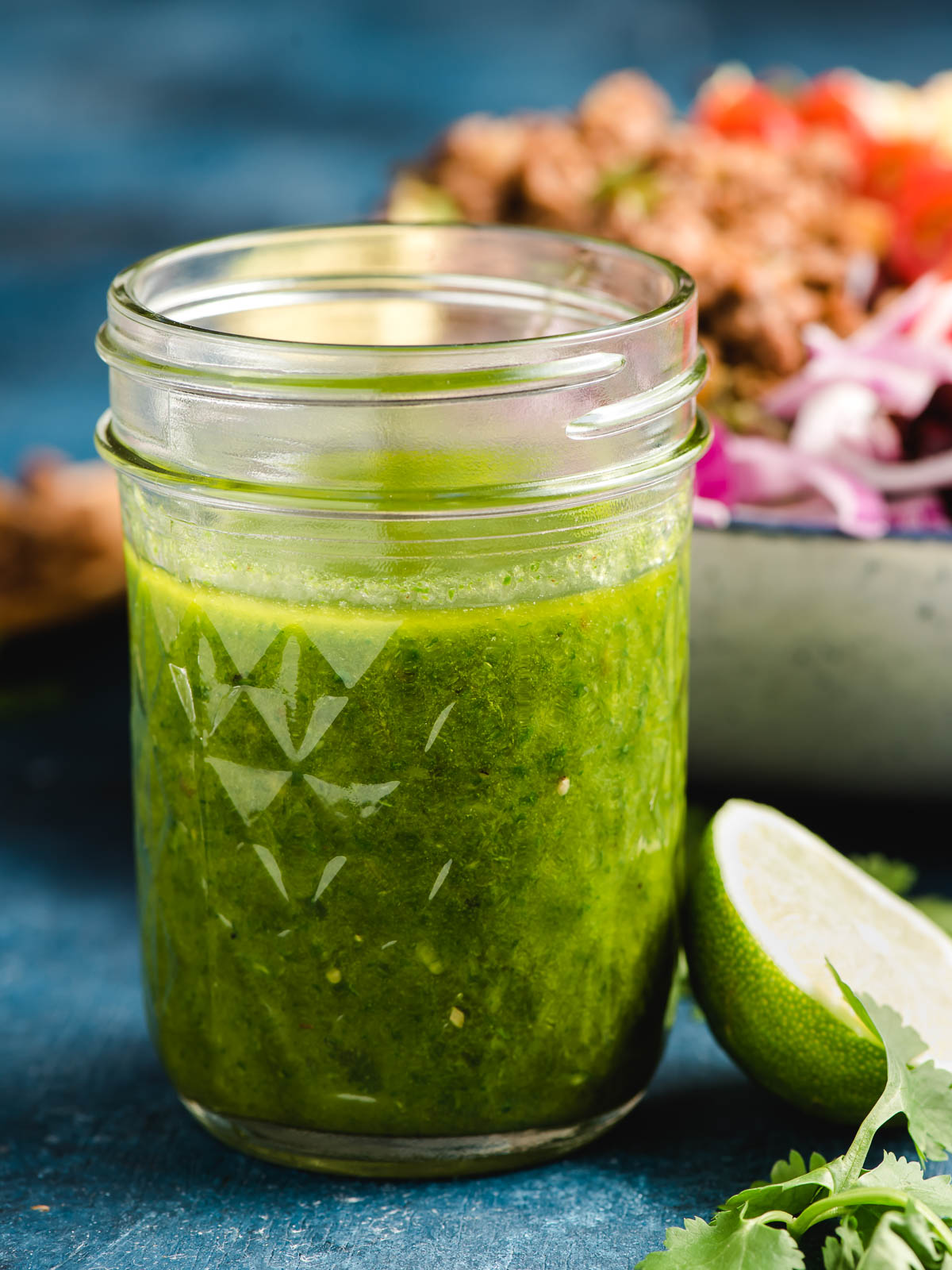 A jar of Cilantro Lime Vinaigrette sits on a table before being poured on taco salad as dressing.