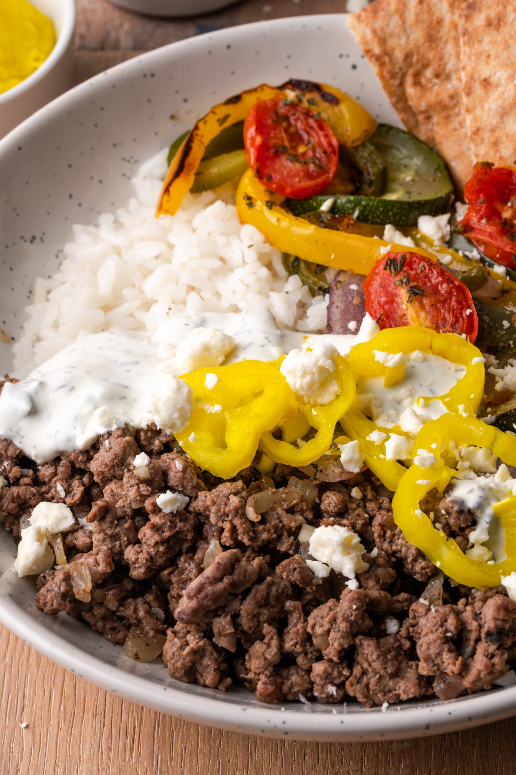Bowl with rice, ground beef gyro meat, banana peppers, feta cheese, and roasted veggies.