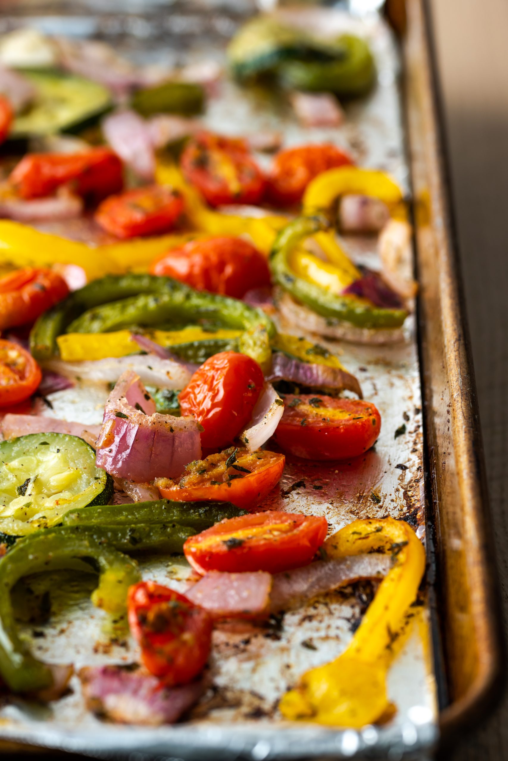 Sheet pan of roasted red onion, tomatoes, peppers, and zucchini.