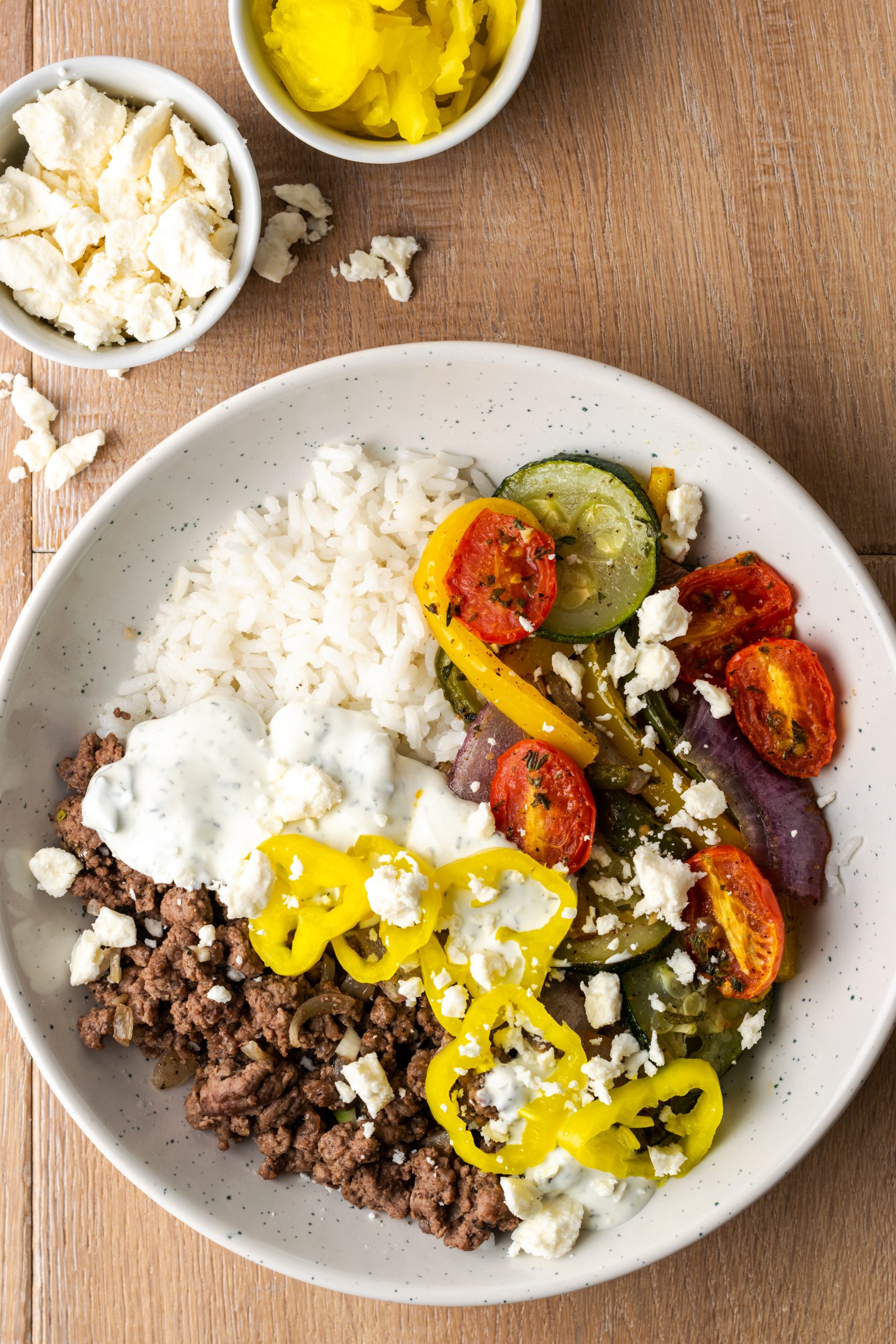 Ground beef gyro bowls shown with banana peppers, roasted vegetables, and feta cheese.