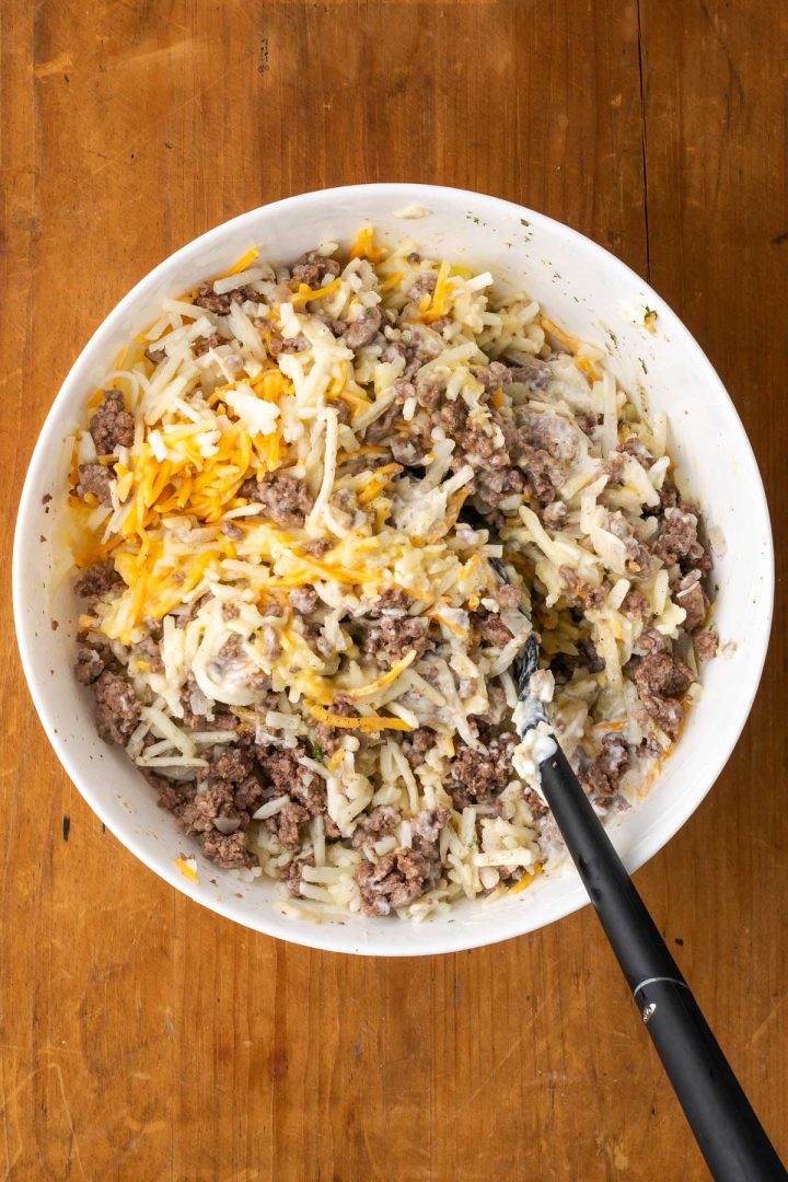Hashbrowns, ground beef, cheddar cheese, condensed soup, and sour cream stirred together in a bowl.