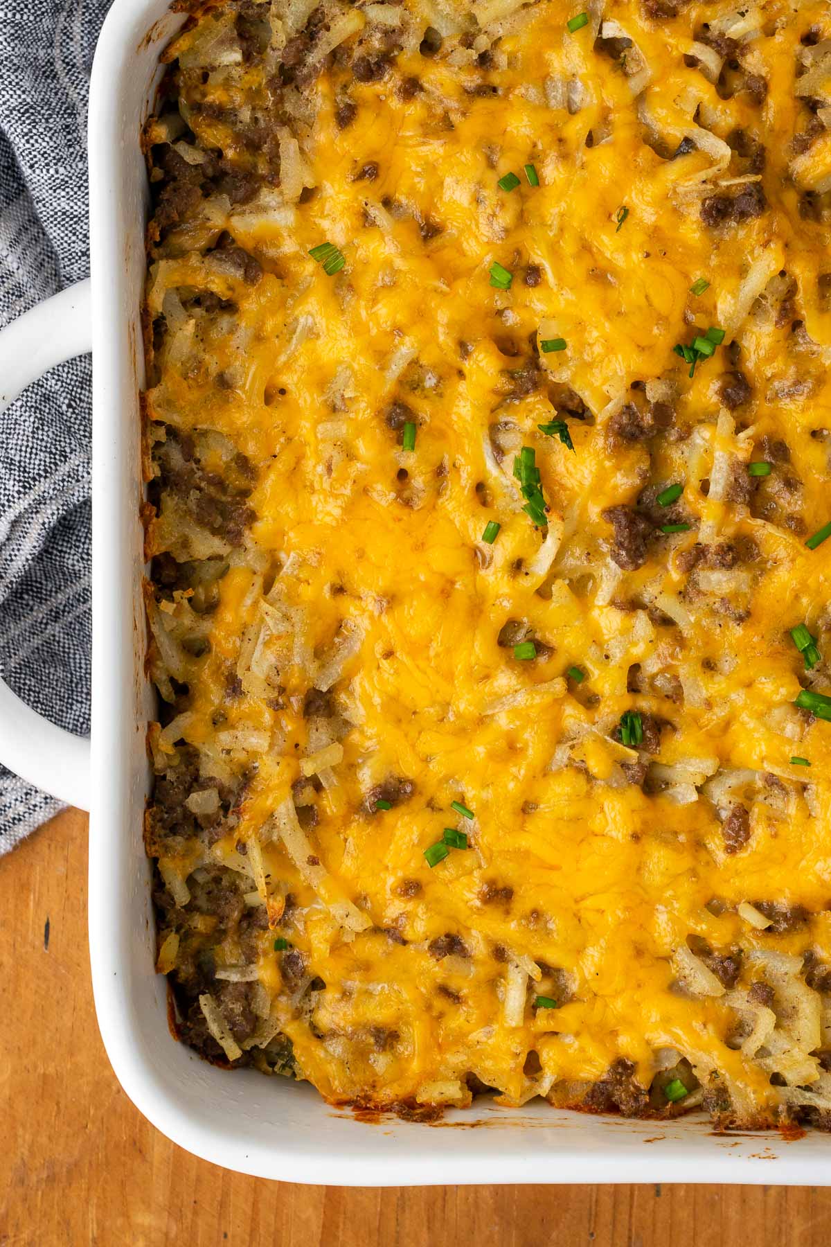 Hashbrown casserole with ground beef and melted cheese shown in a white baking dish.