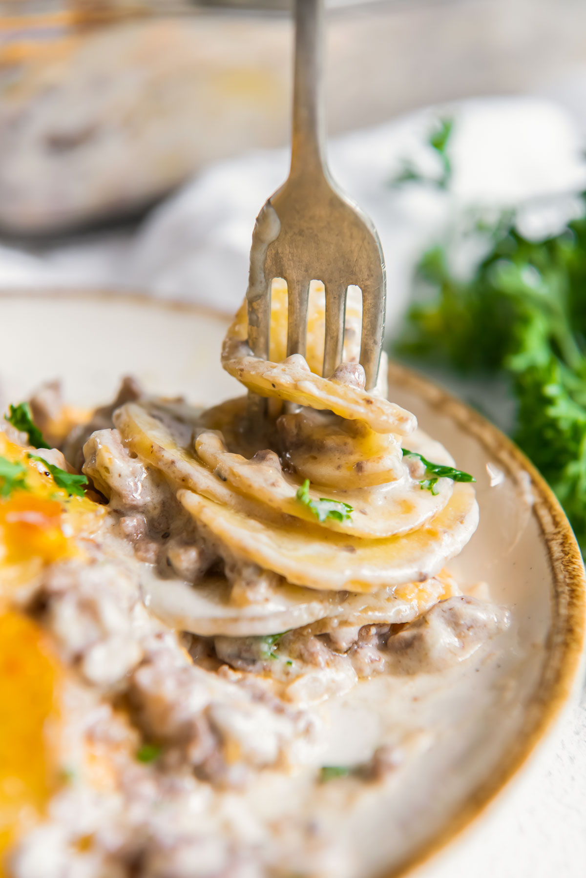 Fork stabbing layers of potatoes and ground beef in a creamy sauce.