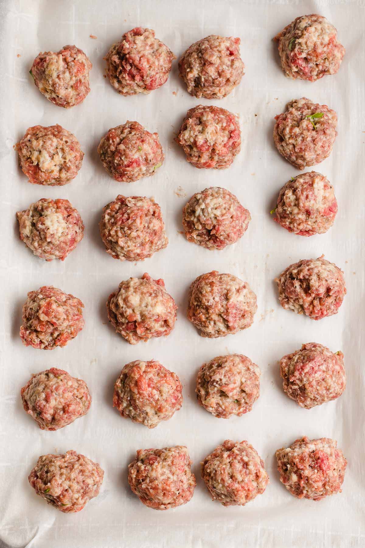 Raw meatballs lined up on parchment paper before baking.