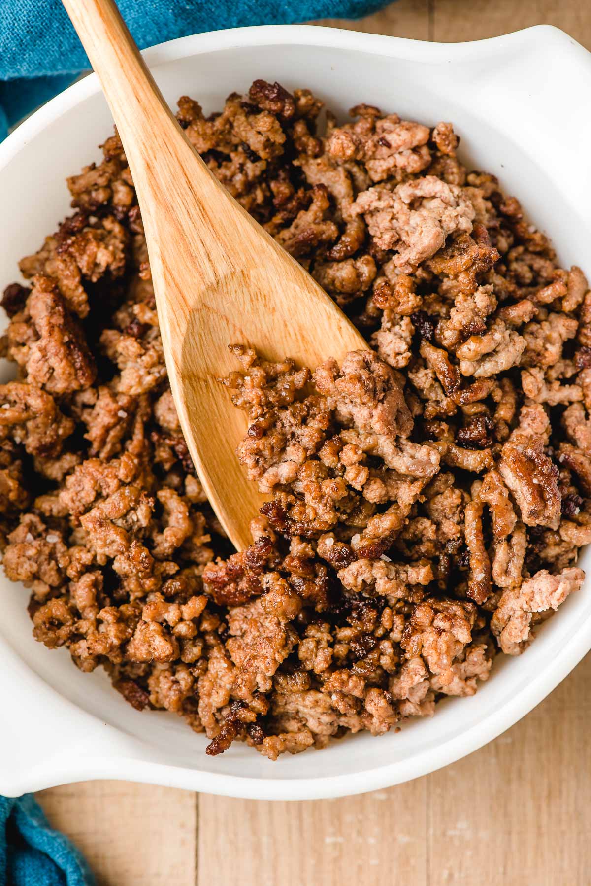Wooden spoon scooping up cooked ground beef.