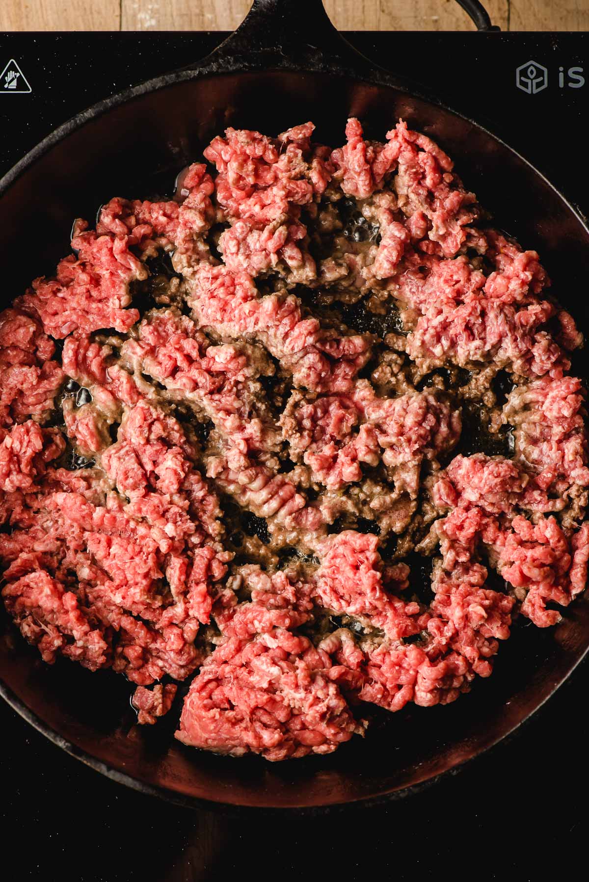 Ground beef browning in a cast iron skillet.