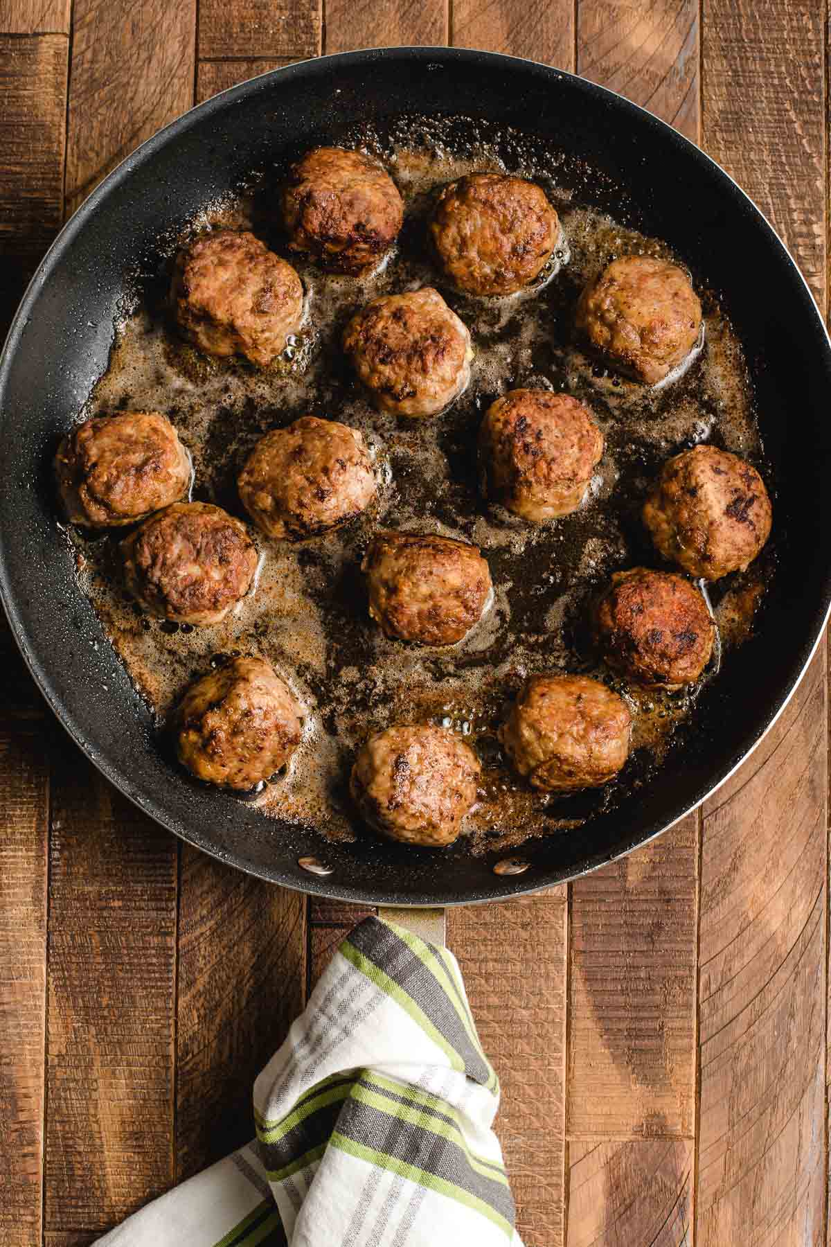 Meatballs frying in a cast iron skillet.