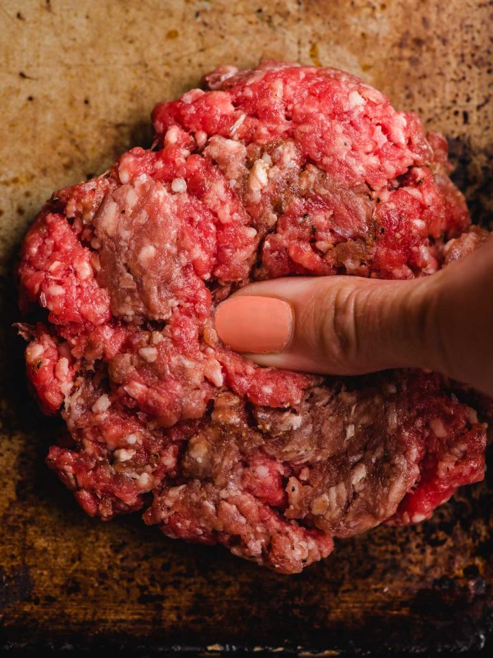 Thumb pressing an indent into the center of a burger patty.