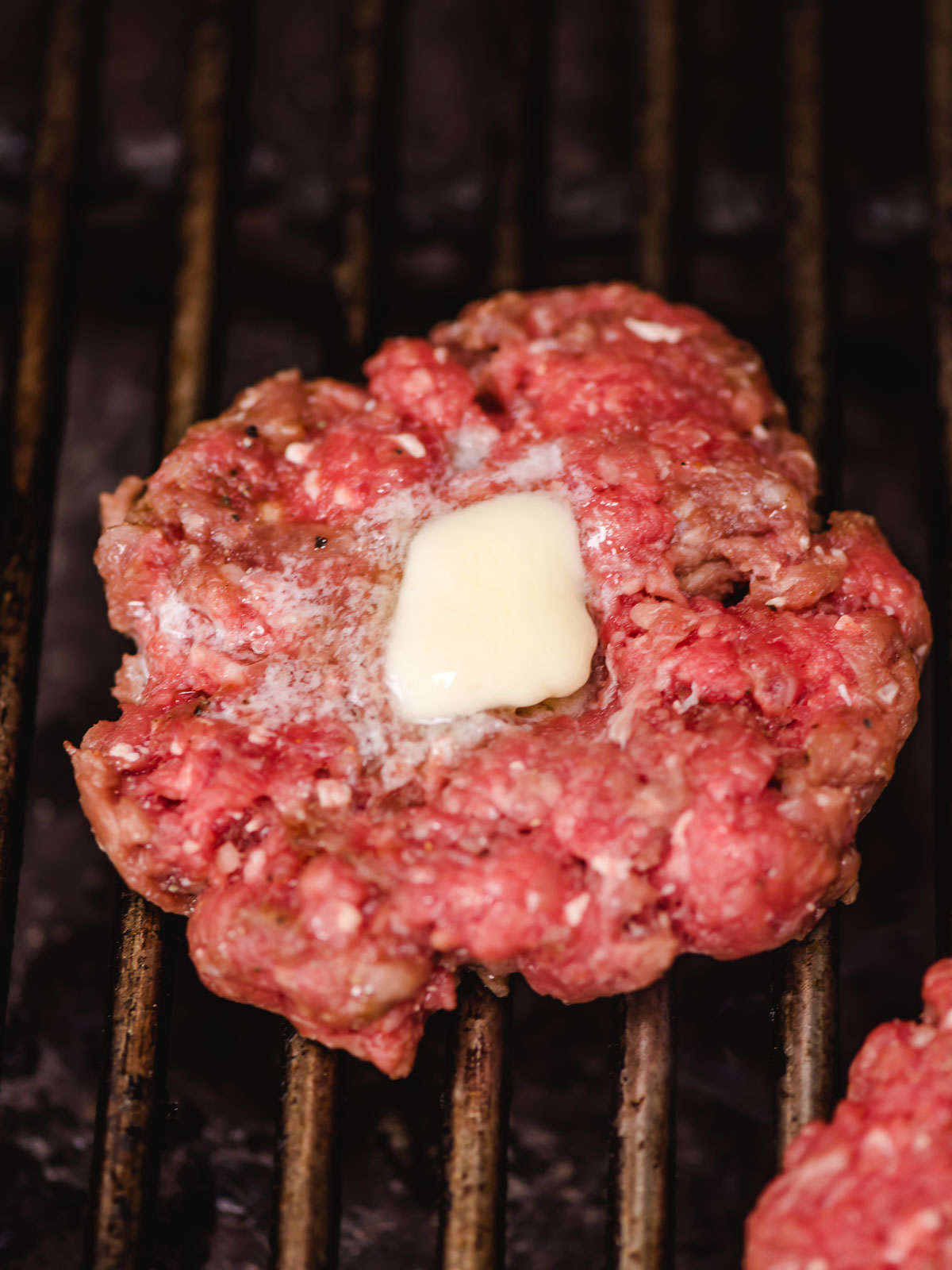 Burger patty shown on a grill with a pat of butter melting on top.