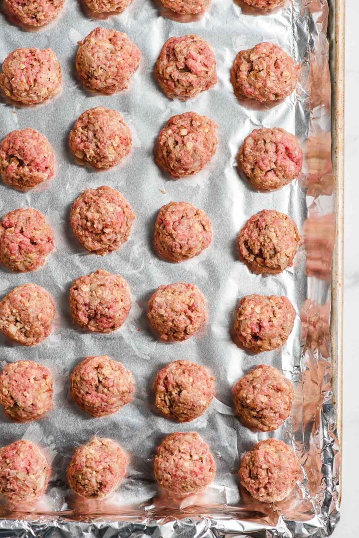 Uncooked homemade meatballs lined up on a baking sheet.