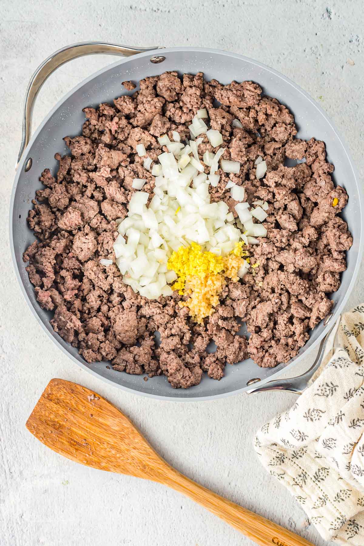 Cooked ground beef in a skillet with onion and garlic shown on top.