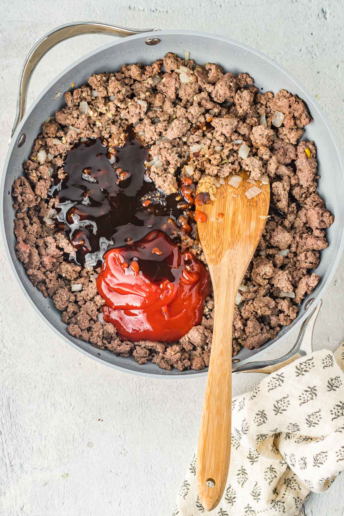Cooked ground beef in a skillet with hoisin sauce and ketchup on top.