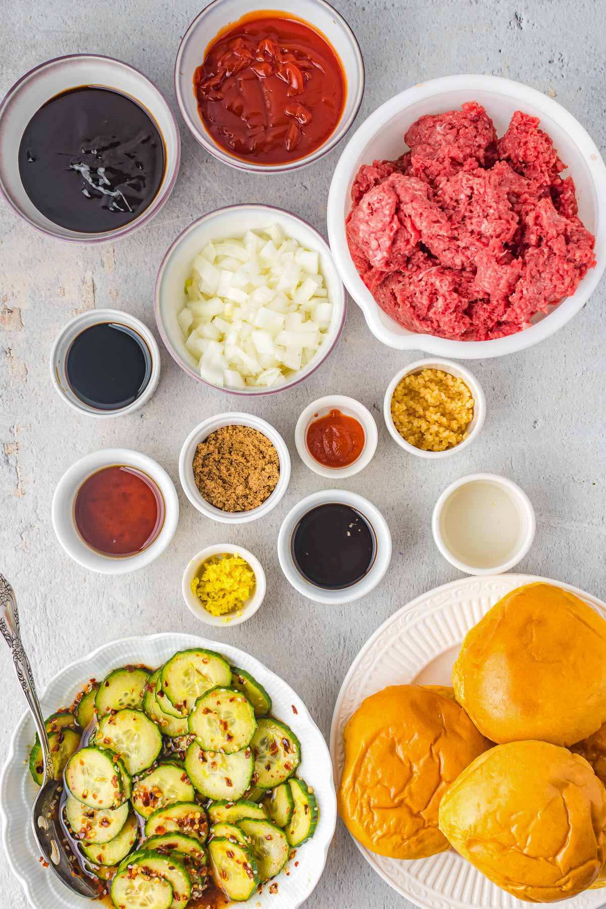 Ingredients for a korean sloppy joe recipe in small bowls, plus a plate with brioche buns and one filled with Korean pickles.