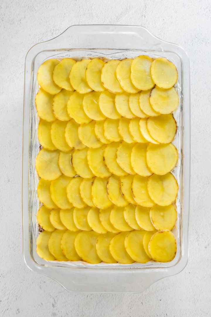 Casserole dish layered with sliced potatoes.