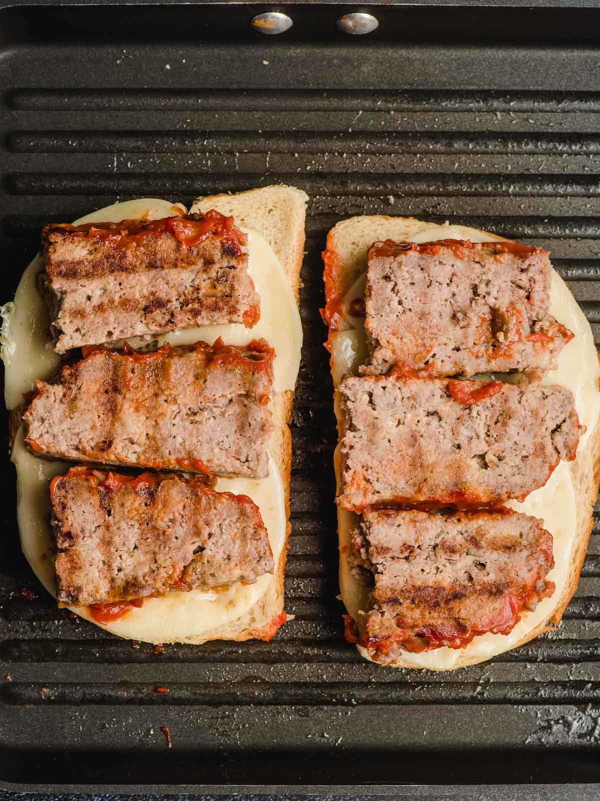 Two halves of a hot meatloaf sandwich on a griddle.