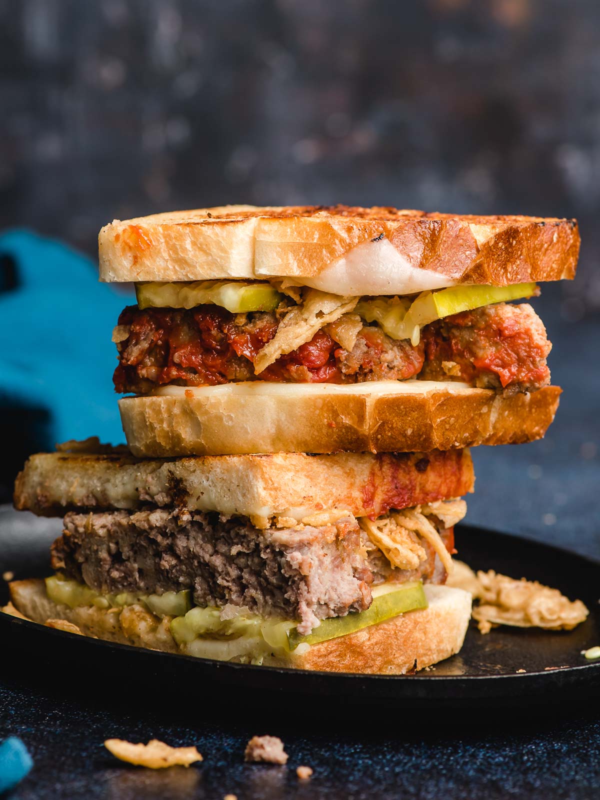 Two halves of a leftover meatloaf sandwich stacked on a plate.