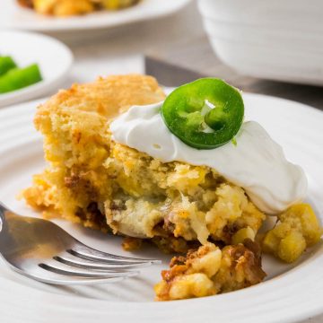 A slice of Mexican Cornbread Casserole topped with sour cream and a jalapeno slice served on a plate.