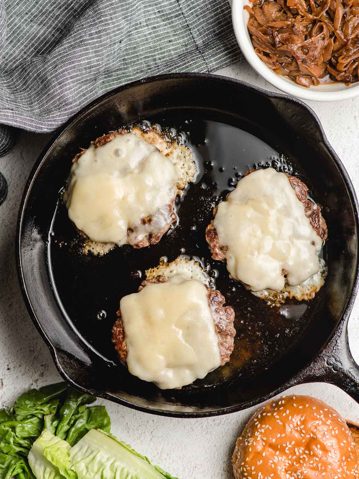 Three burger patties in a cast iron skillet with melted Swiss cheese on top.