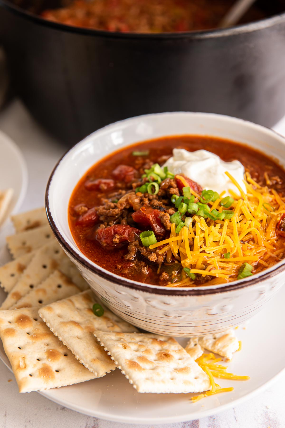 Bowl of chili topped with shredded cheese, sour cream, and green onions.