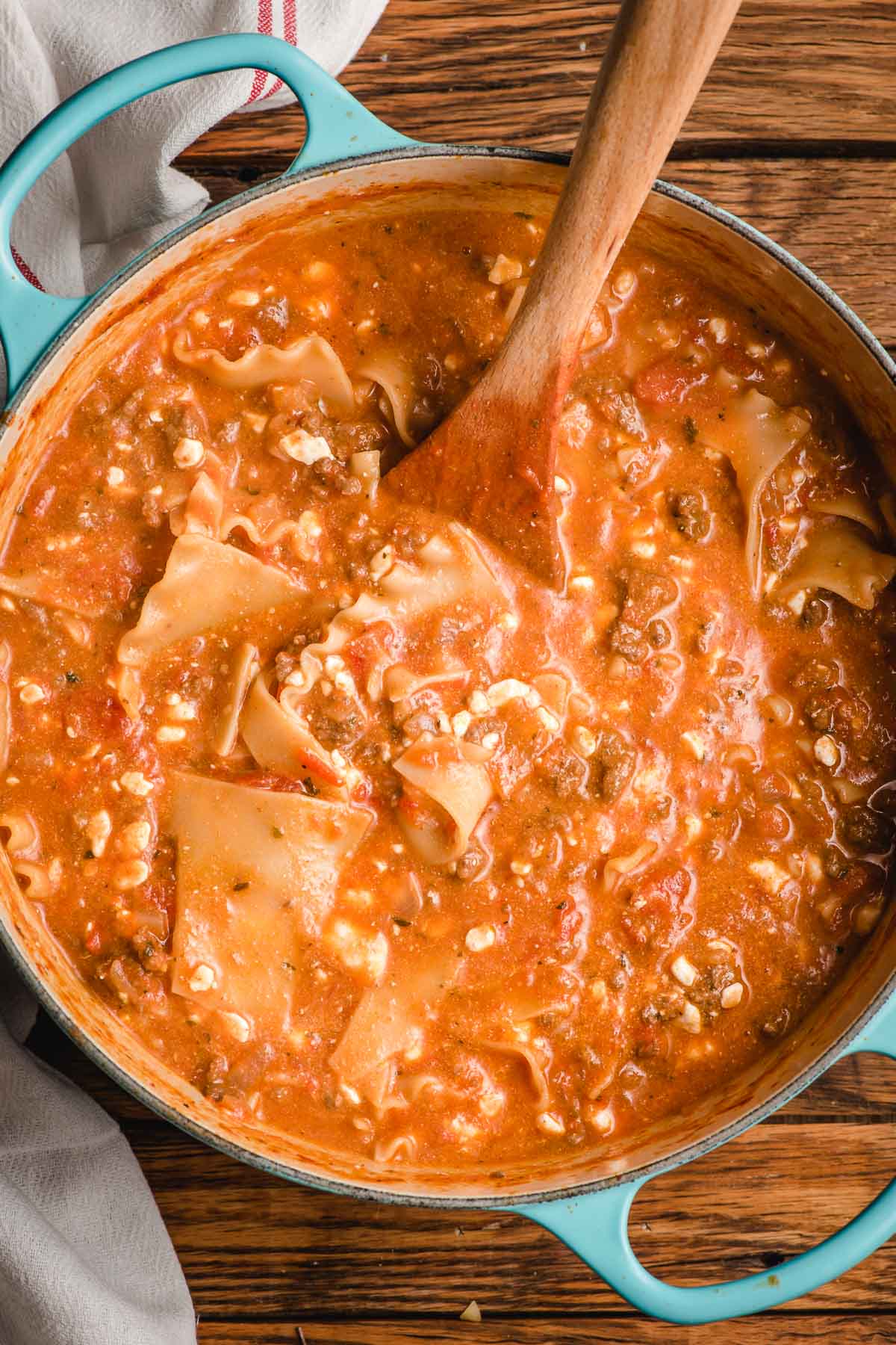 Wooden spoon stirring lasagna soup in a Dutch oven.