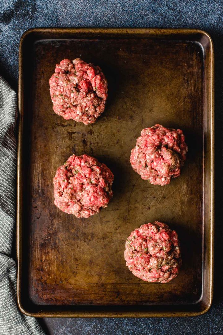Four balls of hamburger meat on a baking sheet before being pressed into patties.
