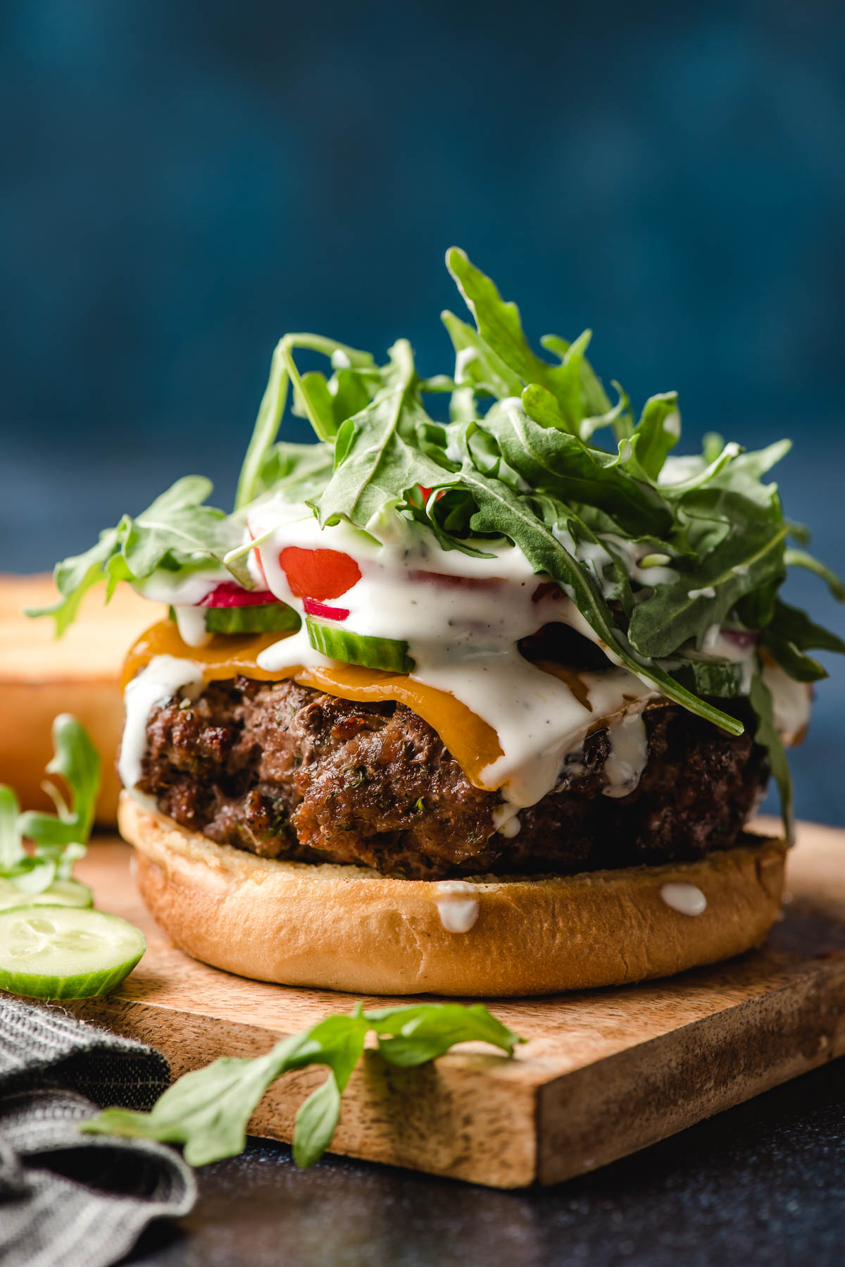 Open face burger topped with cheese, tomato, cucumber, radish, arugula, and Ranch dressing.