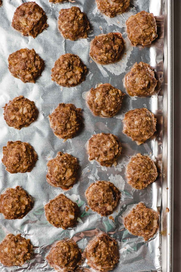Meatballs lined up on a foil lined baking sheet.