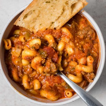 A bowl of slow cooker goulash with hamburger and bread.