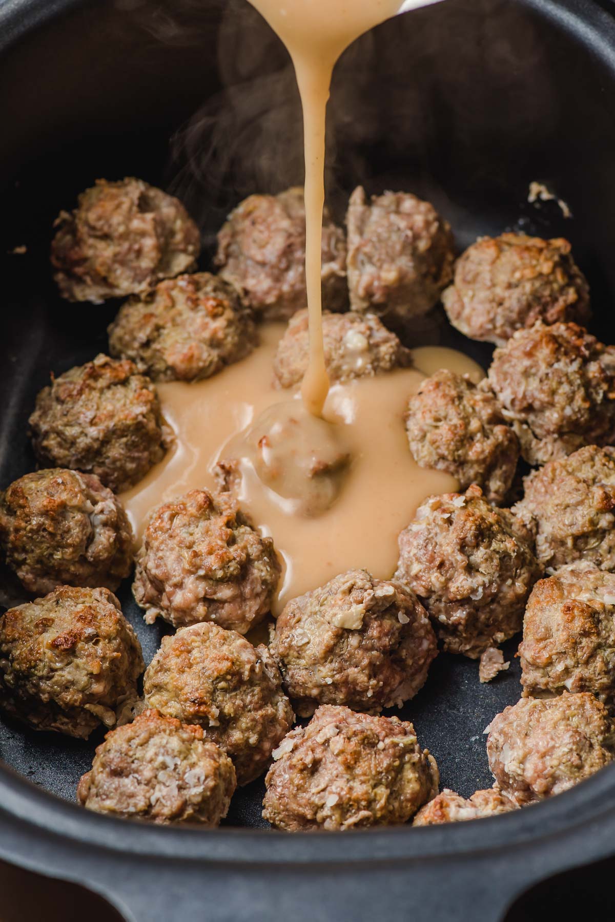 Gravy being poured over meatballs in a slow cooker.