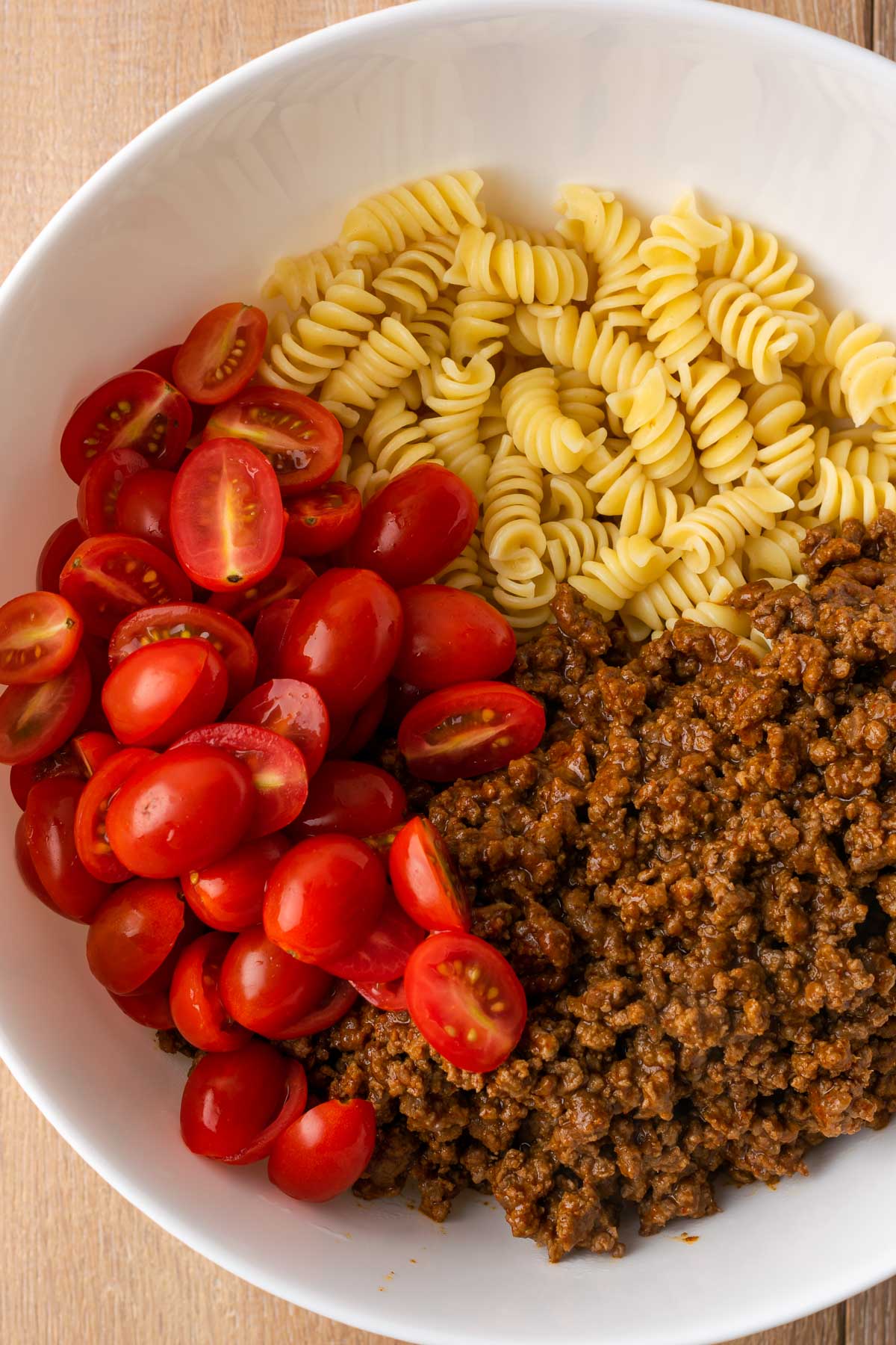Bowl with rotini pasta, sliced grape tomatoes, and cooked taco seasoned ground beef.