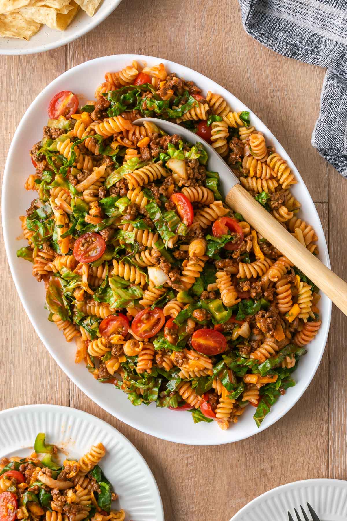 Big spoon, scooping out taco pasta salad from a whtie platter.
