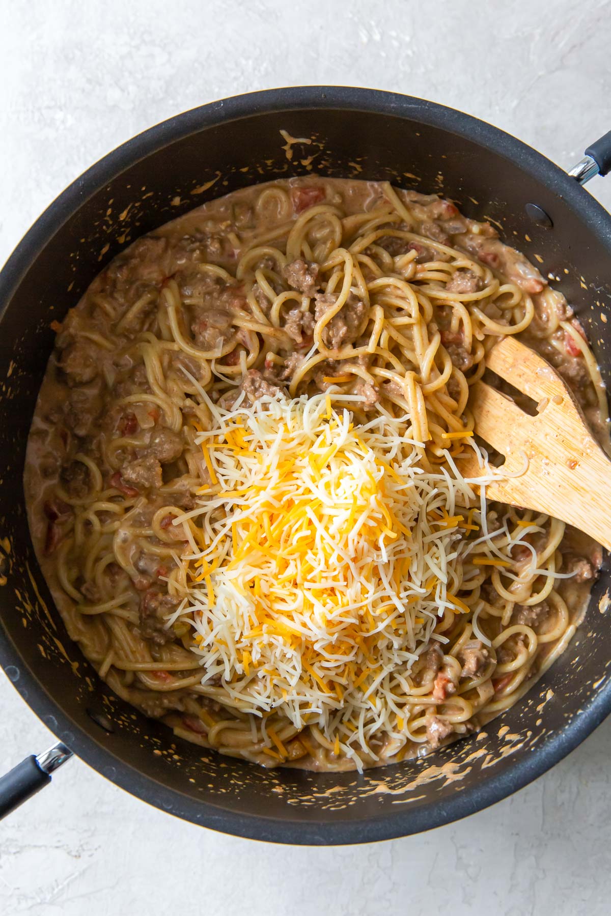 Adding shredded cheese to one pot taco spaghetti.