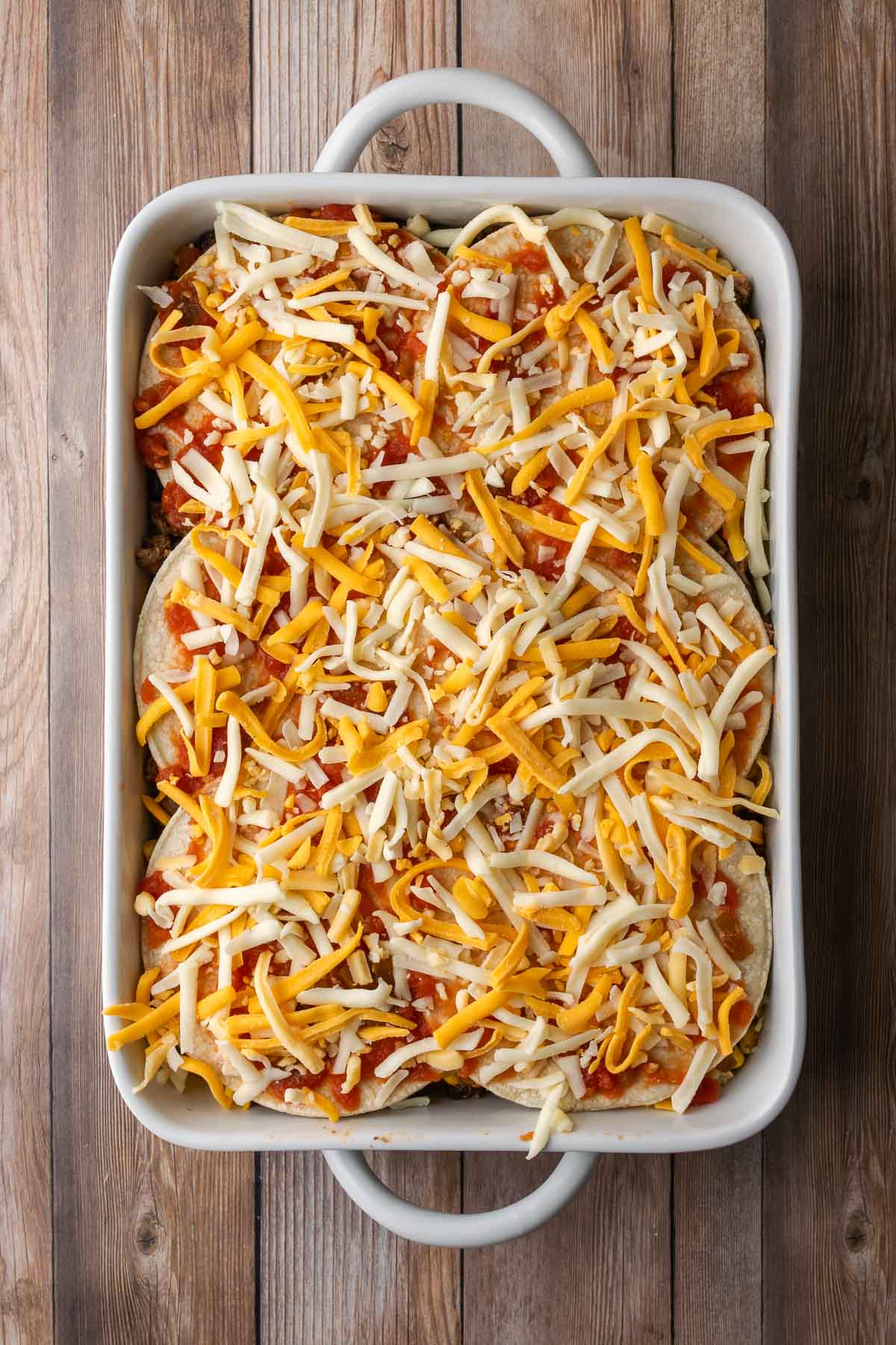 Unbaked tortilla lasagna topped with lots of shredded Mexican blend cheese.
