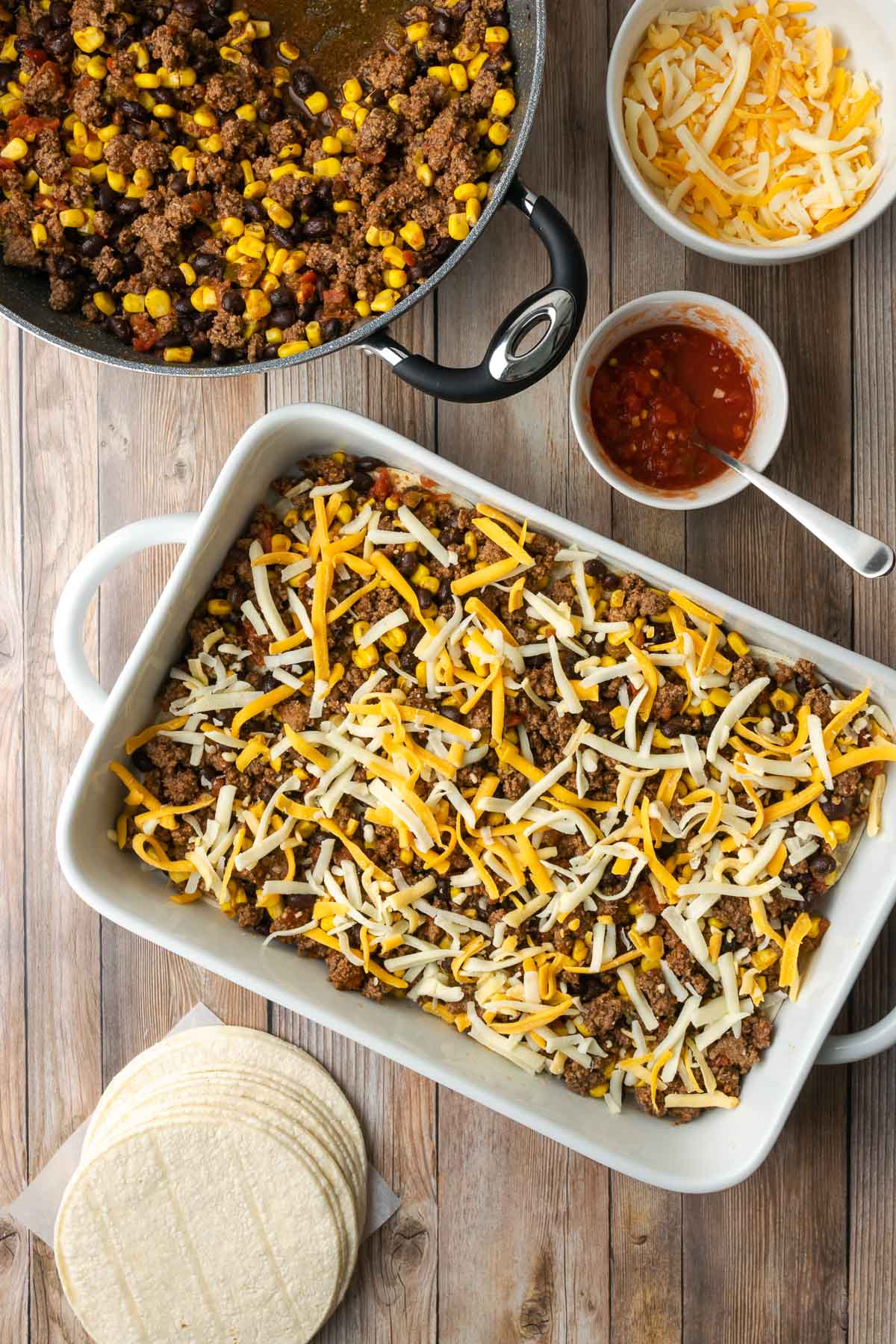Casserole filled with tortilla lasagna fixings, with shredded cheese on top.