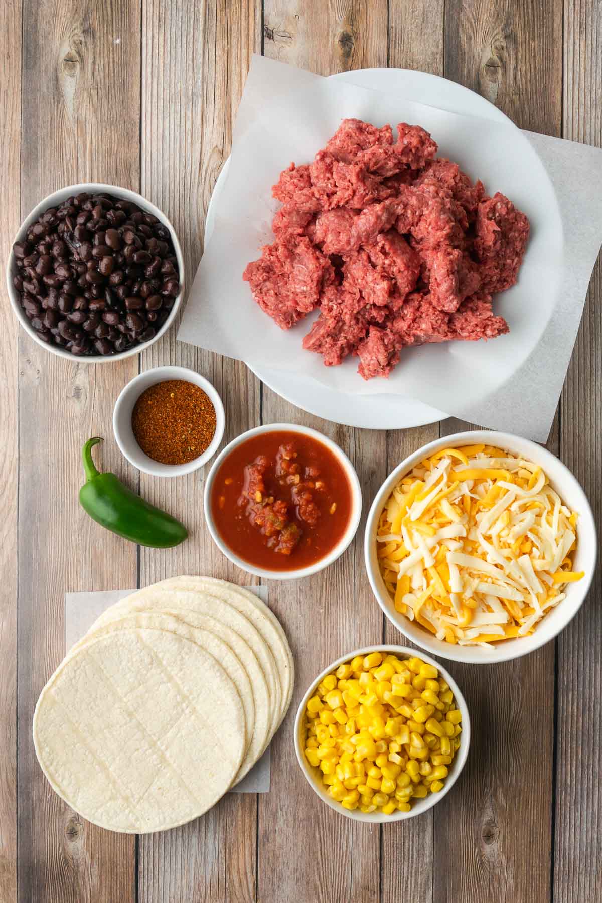Ingredients for Mexican lasagna including tortillas, corn, salsa, cheese, ground beef, and black beans.